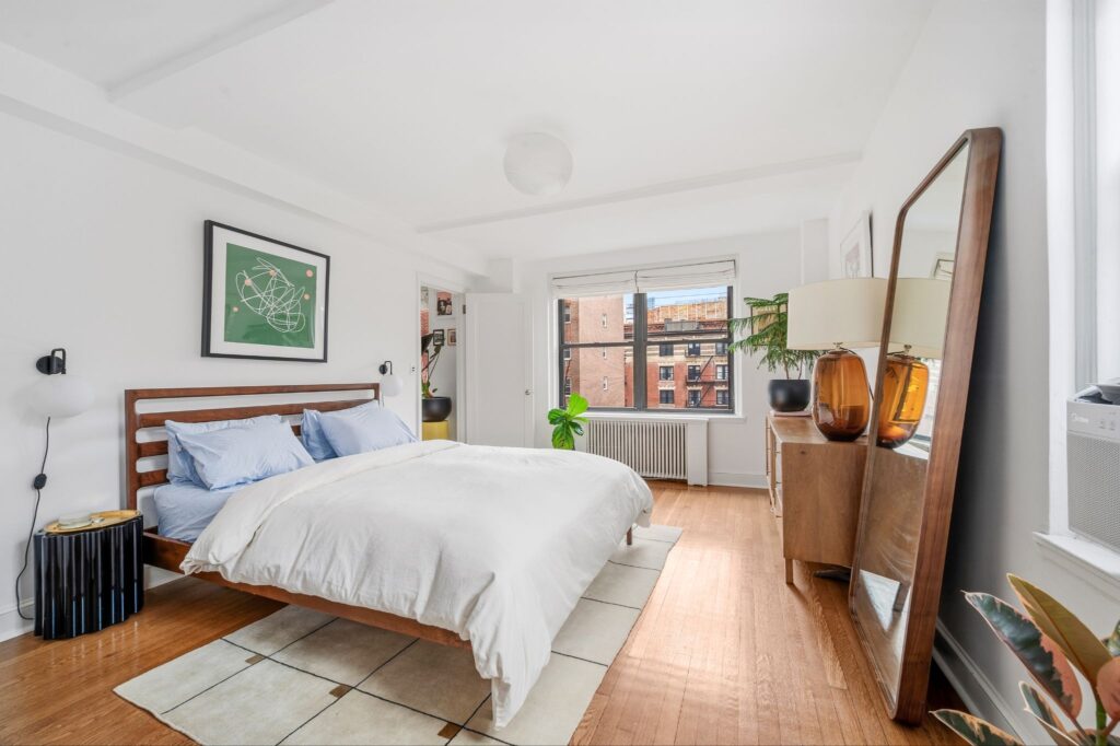 Chambre d'avant-guerre ensoleillée avec parquet, grand miroir au sol et vue dégagée sur la ville au 140 East 28th Street à Manhattan, New York.