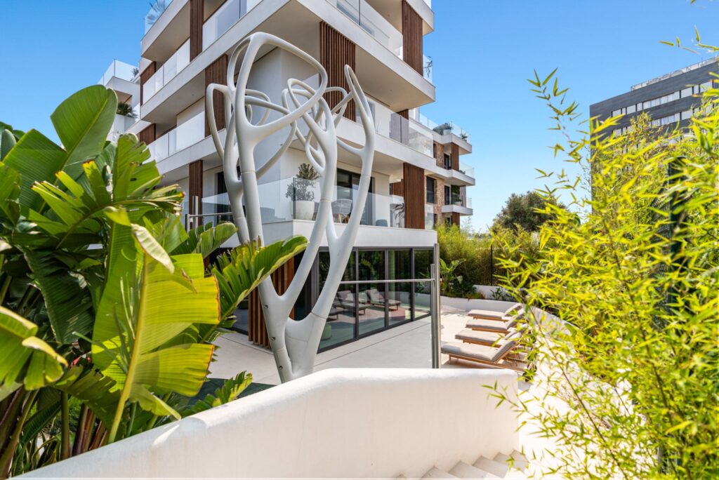Extérieur d'appartement dynamique de nouvelle construction à Playa d'en Bossa, Ibiza, présentant une architecture moderne, un aménagement paysager tropical et une terrasse de piscine ensoleillée.