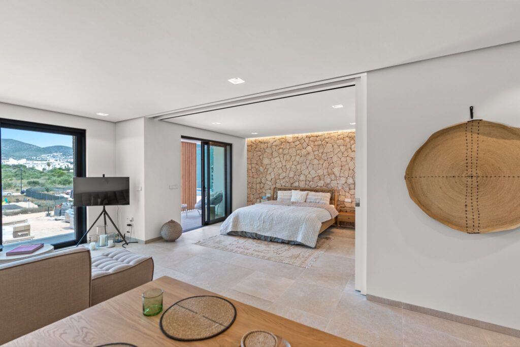 Appartement moderne d'une chambre à coucher à Playa d'en Bossa, Ibiza, avec des portes coulissantes escamotables, un mur d'accent en pierre texturée et un aménagement ouvert.