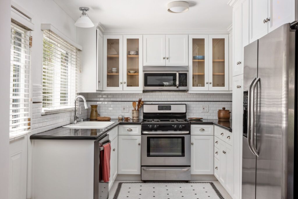Cuisine blanche en forme de U mise à jour avec des appareils électroménagers en acier inoxydable, des comptoirs sombres, un dosseret en carrelage de métro blanc et un sol carrelé au 22051 Celes Street à Woodland Hills, en Californie.