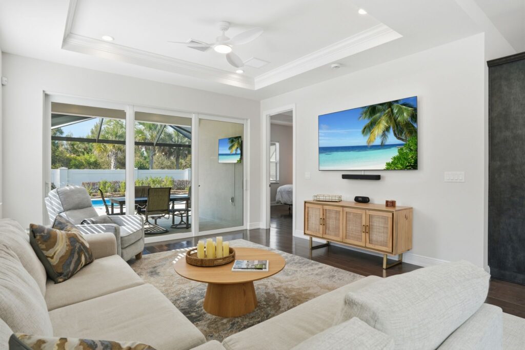 Salon lumineux à aire ouverte avec un plafond à plateau et des portes coulissantes en verre ouvrant sur une véranda avec moustiquaire au 9194 Cayman Drive à Naples, en Floride.
