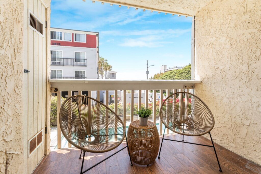 Patio couvert et aéré au 22 Navy Street à Venice, en Californie, doté de chaises en glands tressés, d'un parquet d'aspect bois et d'une vue sur la piscine chauffée et le spa communautaires.