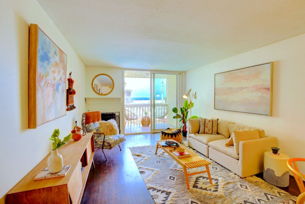 Salon bohème à aire ouverte avec une cheminée en brique et une porte coulissante en verre menant à un patio avec vue sur la plage au 22 Navy Street à Venice, en Californie.